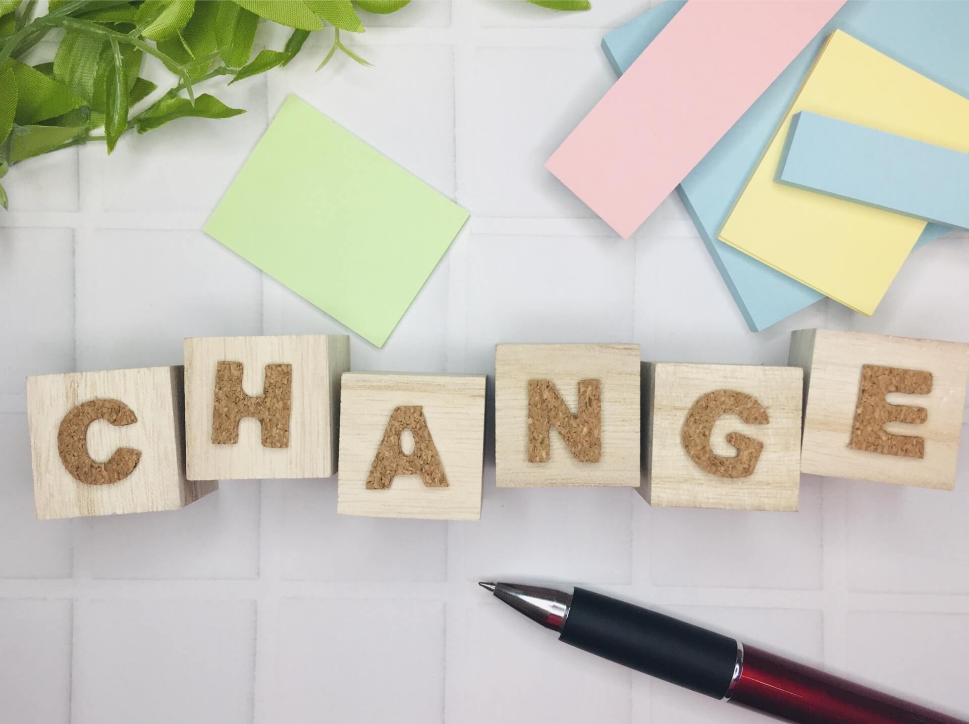 木製ブロックで「CHANGE」と綴られた文字とカラフルな付箋、ペンが並ぶ画像。変化やイメチェンをイメージさせる構図。