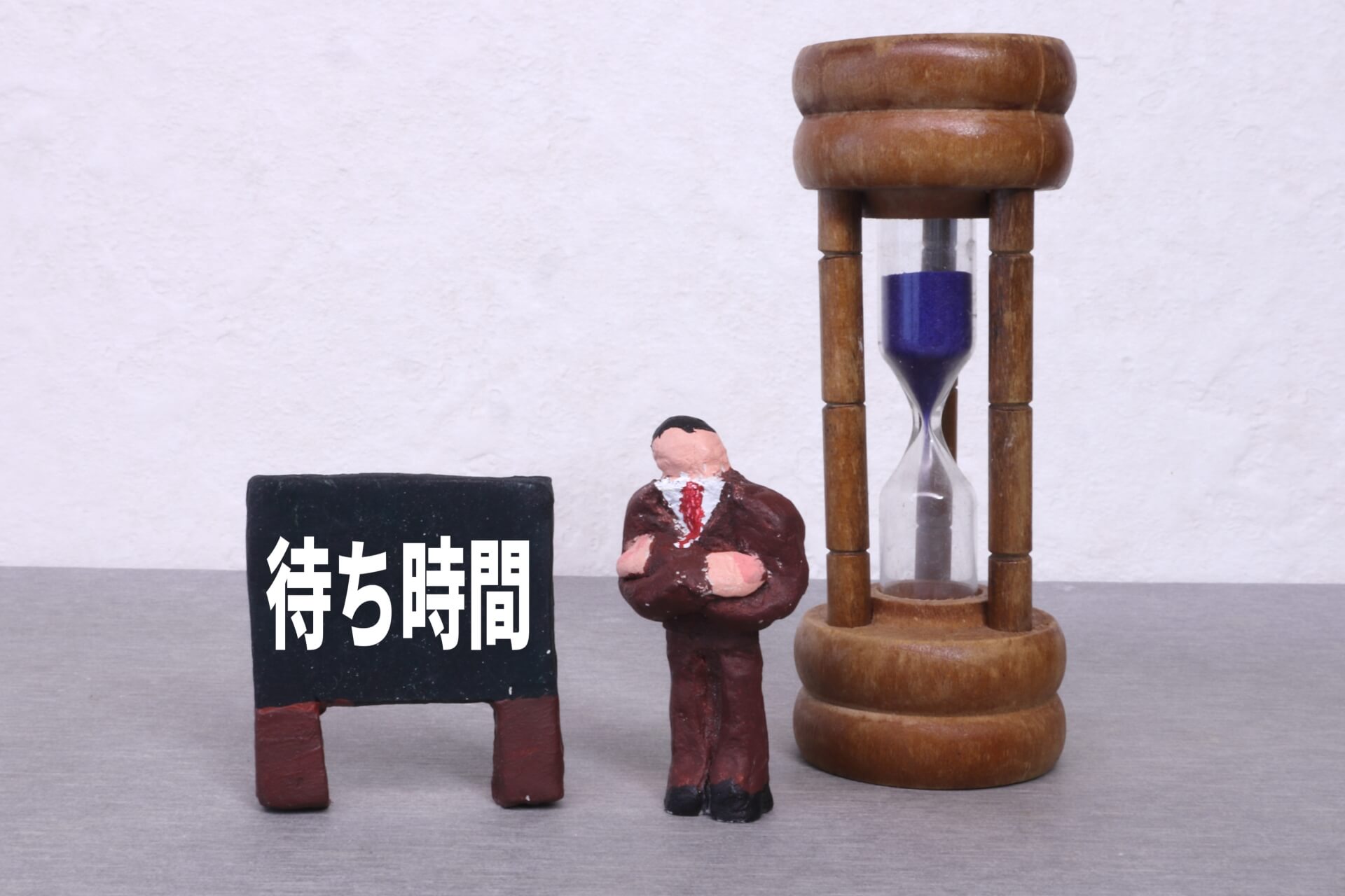 砂時計と腕を組んで待っているスーツ姿の男性の粘土人形。そばには「待ち時間」と書かれた黒板が置かれている。