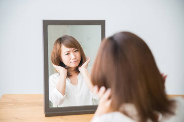鏡を見ながら毛先のはねに悩む女性