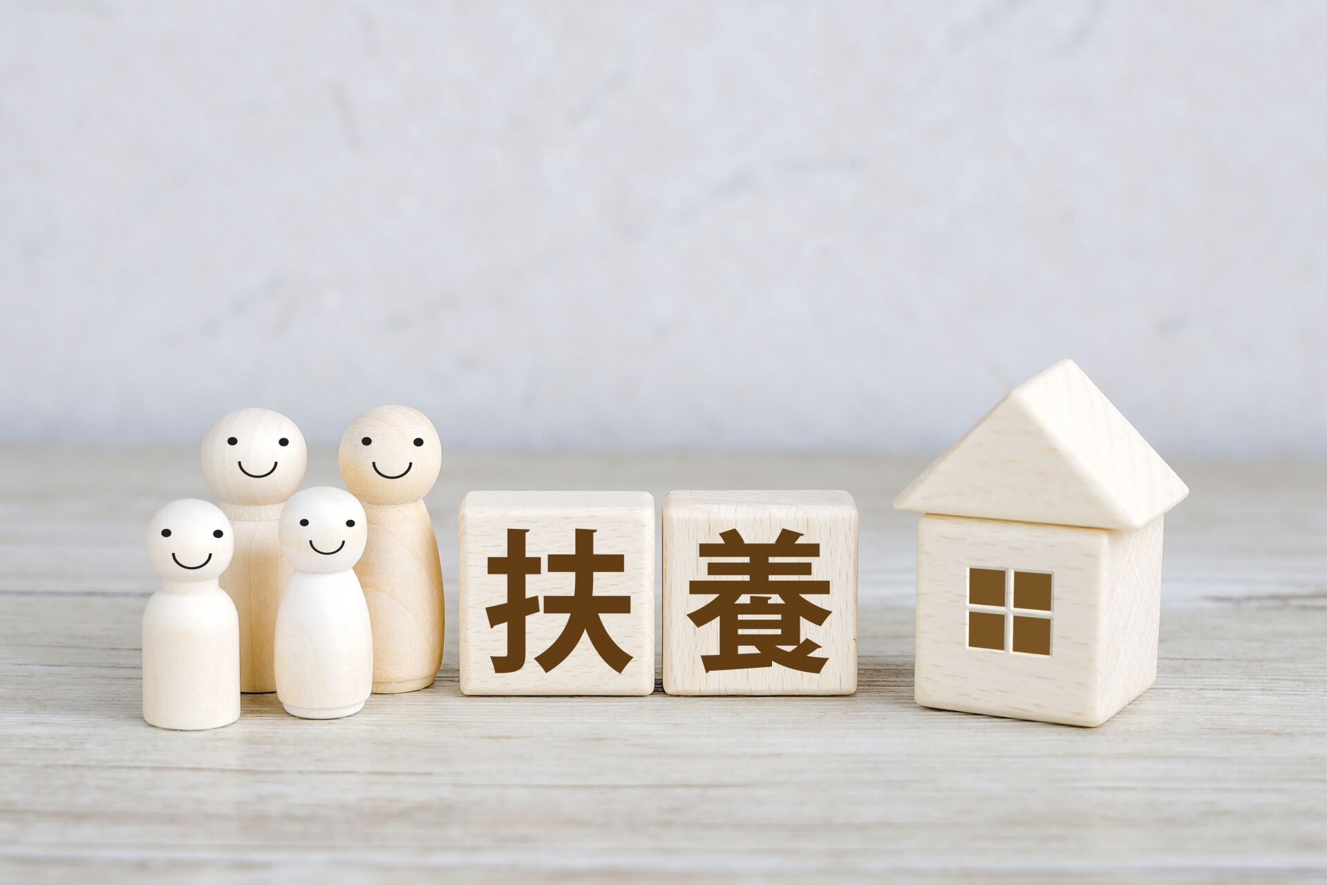 扶養に関するイメージ。家族と住宅を表す木製オブジェと「扶養」の文字が並ぶ。