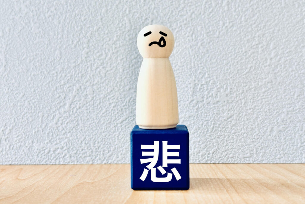 美容室選びに失敗して悲しんでいる様子を表す泣き顔の人形と「悲」の文字ブロック