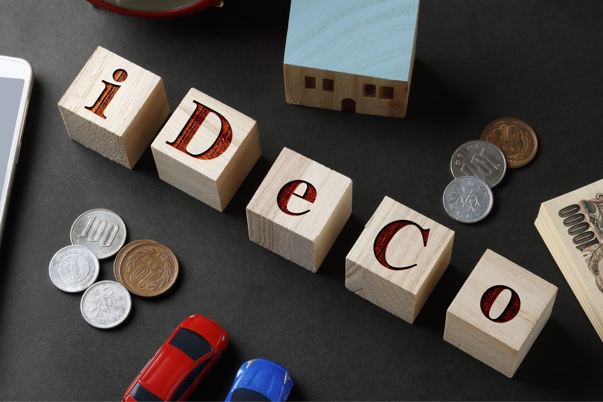iDeCoの文字が描かれた積み木と日本円硬貨や紙幣のイメージ。2024年12月の制度改正で掛金上限2万円・加入年齢70歳未満に拡充