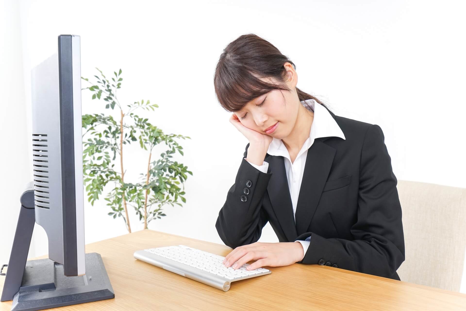 睡眠不足でデスクワーク中に眠そうにしている女性会社員