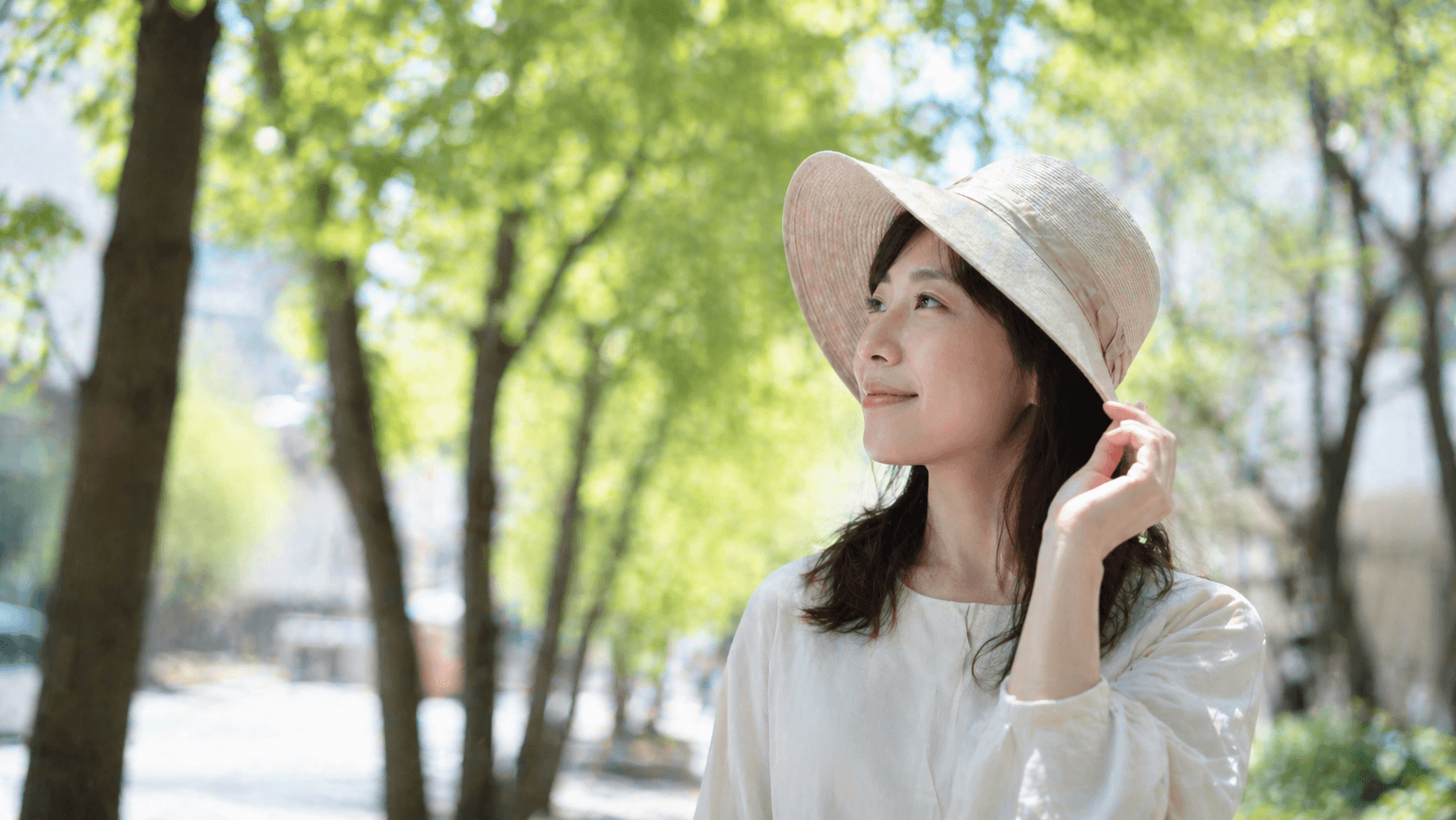 髪の紫外線対策をする女性 つば広帽子で日差しを遮る