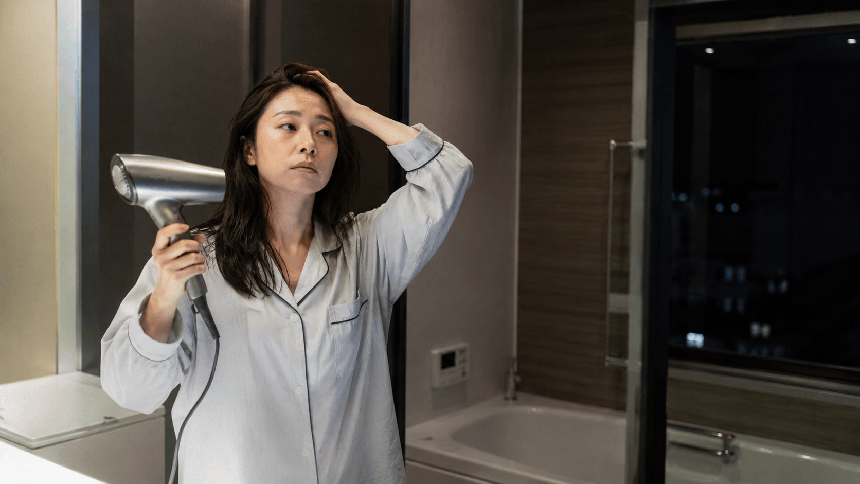 髪を乾かさないで寝るとどうなるか考える女性